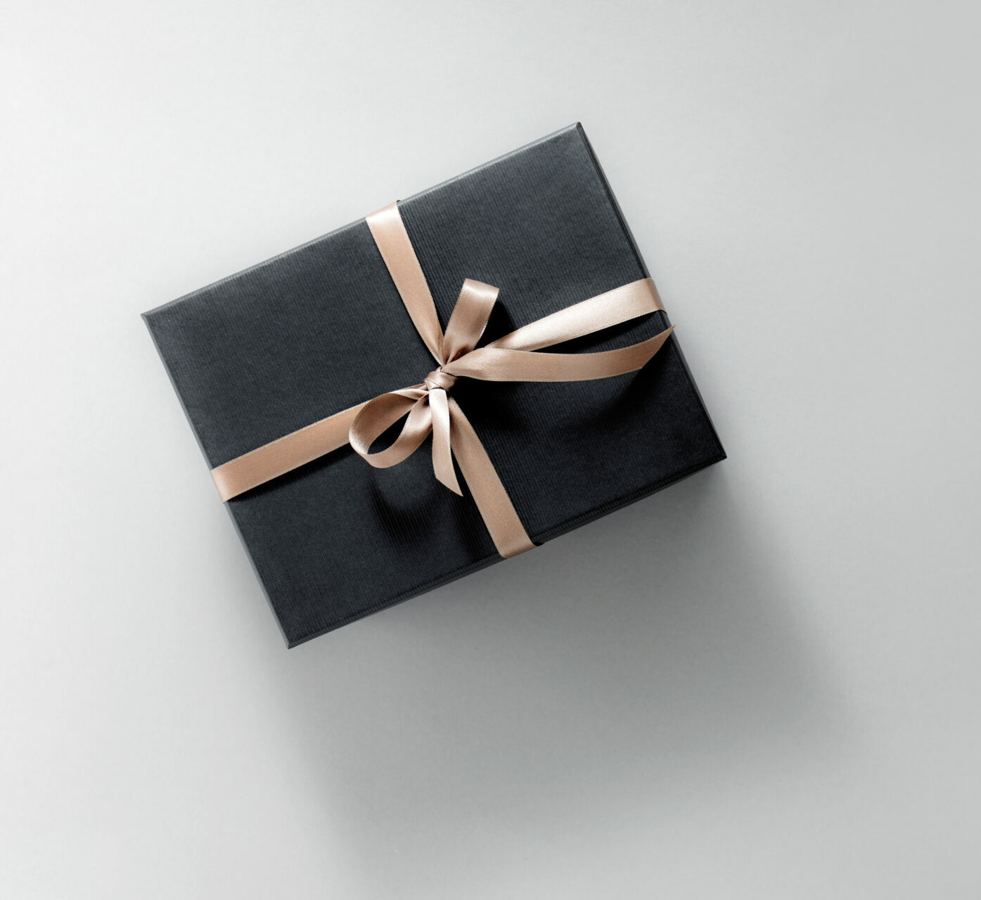 One gift wrapped in dark black paper with luxury bow on pastel background. Horizontal with copy space. Banner